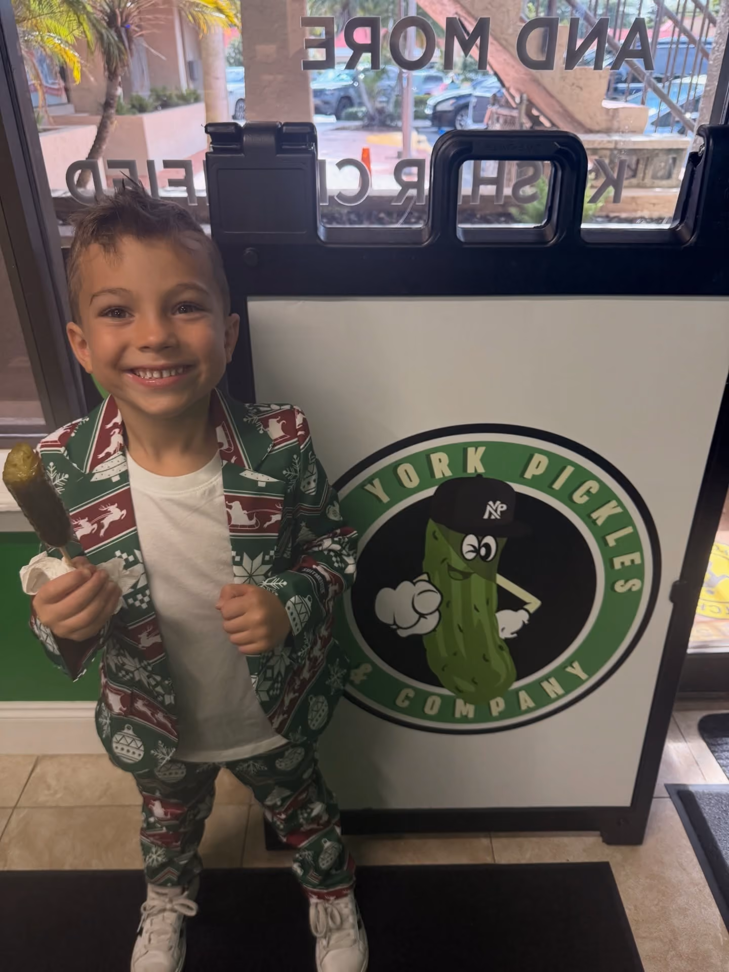 Smiling child in holiday suit holding a pickle in front of a York Pickles Company sign.