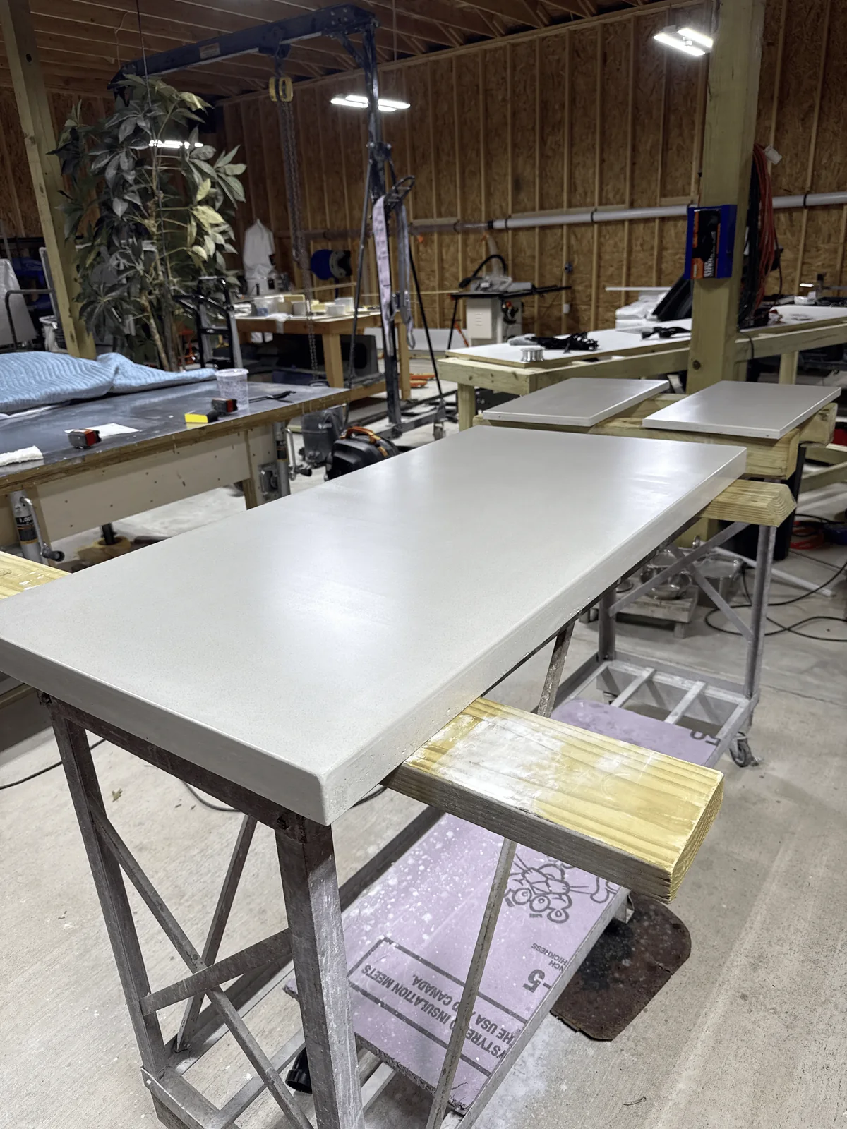 Hand-cast concrete countertop slabs curing on steel trestles in Kennedy's Bastrop shop, with two smaller pieces on the bench behind