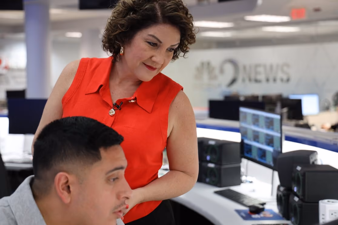 Reporter in red collaborates with a colleague at monitors in a 9NEWS newsroom.