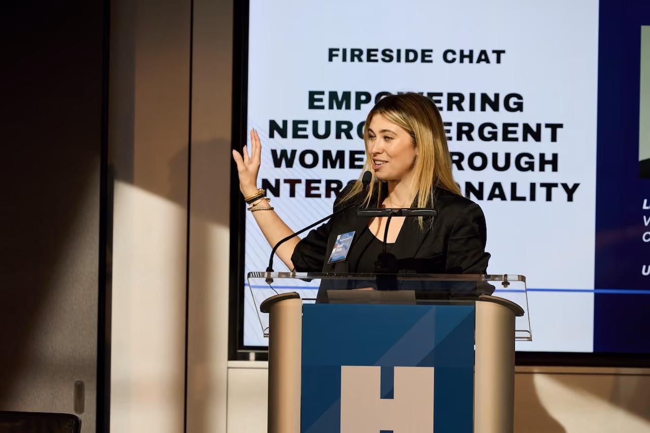 Blonde speaker at a Hearst lectern before a Fireside Chat presentation slide.