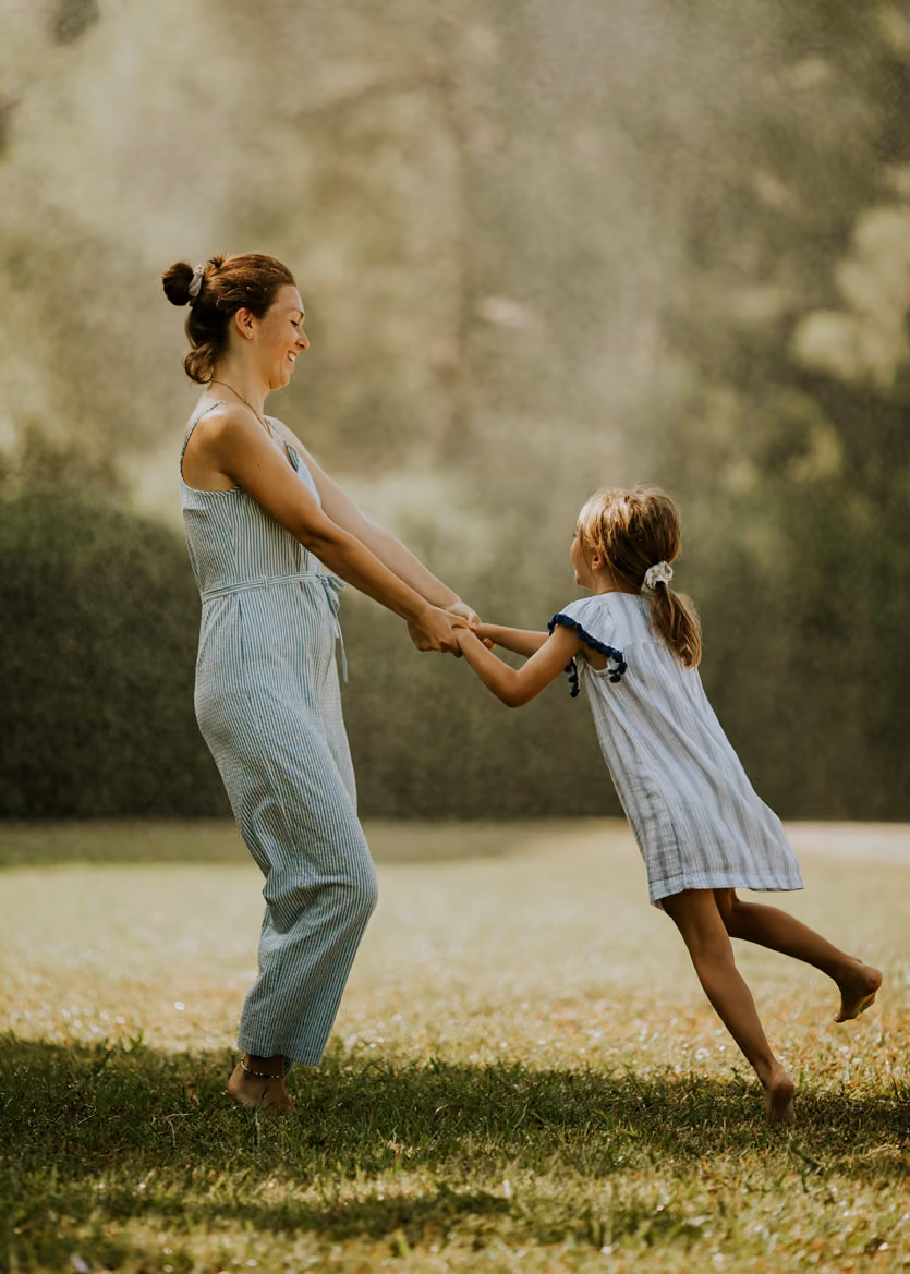 Mother and daughter holding hands, spinning and playing barefoot on grass outdoors.