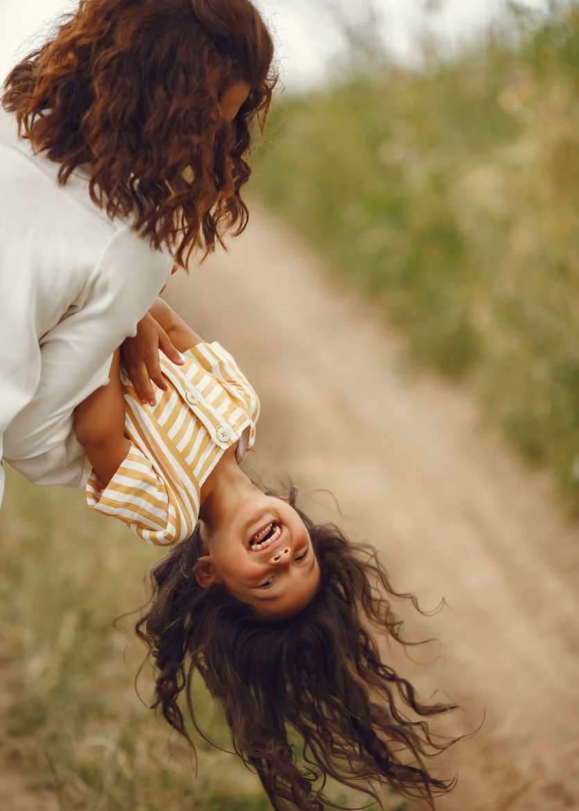 Mother holding her laughing daughter upside down in a green field outdoors.