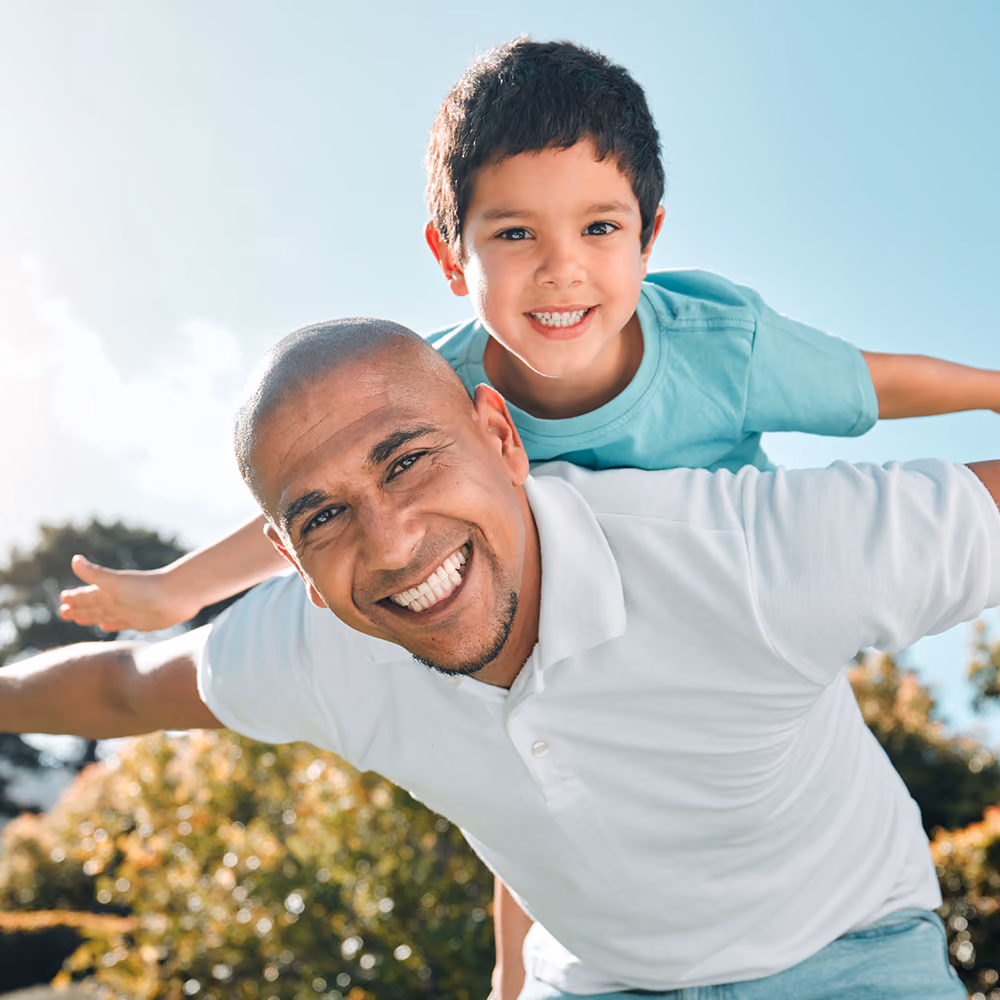 Father and son smiling at camera while son rides fathers back. Therapy with Aaron Helm in Plano, TX