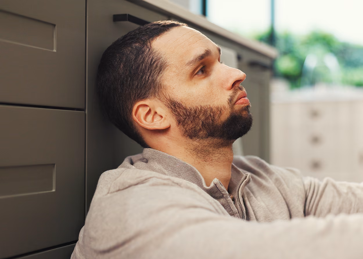 A thoughtful man leans against a cabinet after his partner called him a narcissist, wondering what to do next.