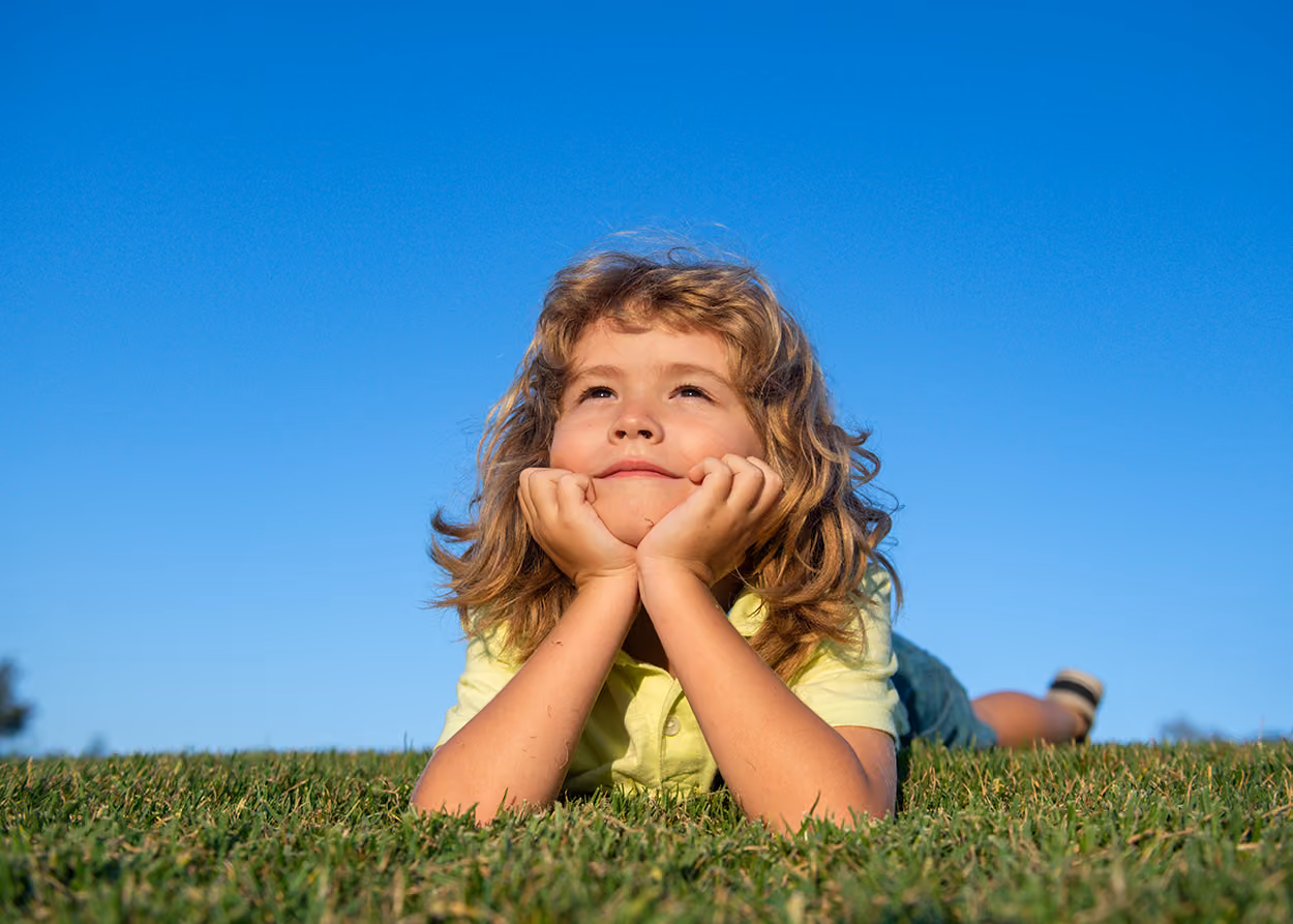 child looking laying in grass looking up at sky. Signs Your Child Needs Play Therapy in Plano, TX (and Signs They Don't)