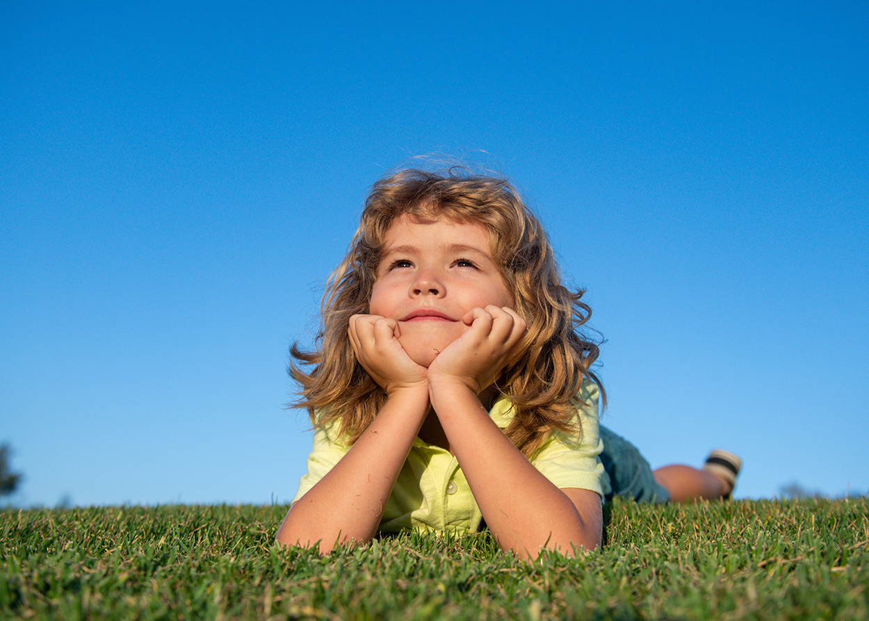 child looking laying in grass looking up at sky. Signs Your Child Needs Play Therapy in Plano, TX (and Signs They Don't)