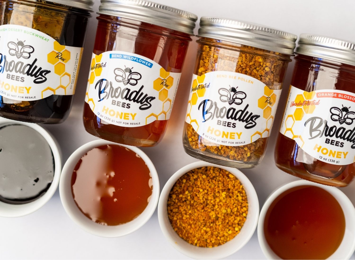 Four jars of Broadus Bees honey and pollen with matching bowls of honey and pollen below each jar.