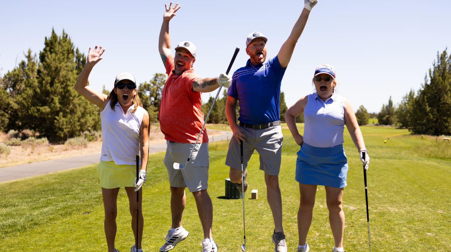 Four golfers on a green course celebrating joyfully with raised arms and golf clubs.