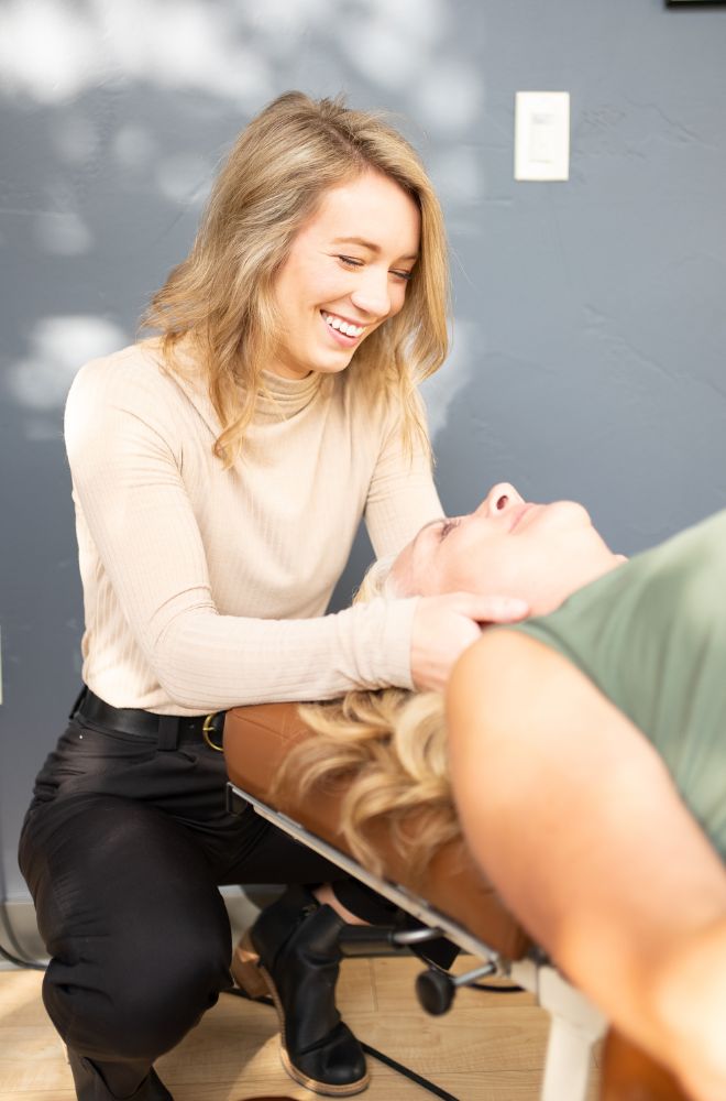 Smiling woman adjusting the head of a relaxed woman lying on a treatment table.