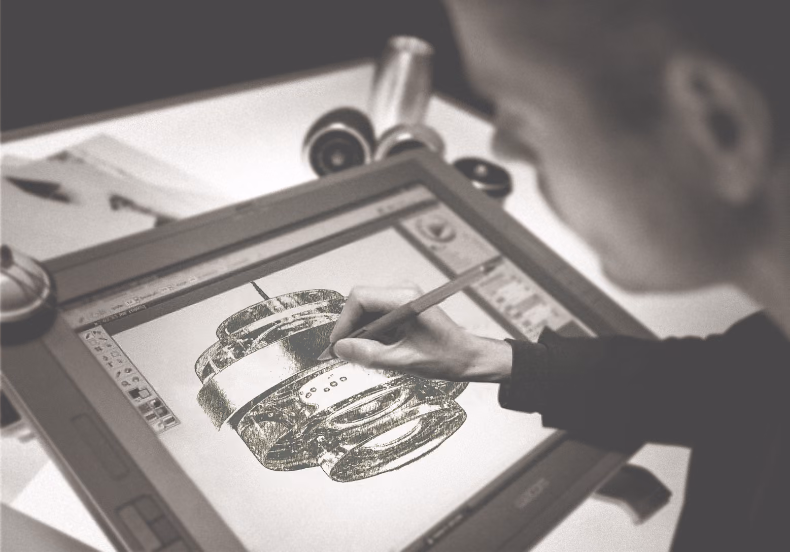 Person using a stylus to draw a detailed mechanical object on a digital pen display tablet on a desk.