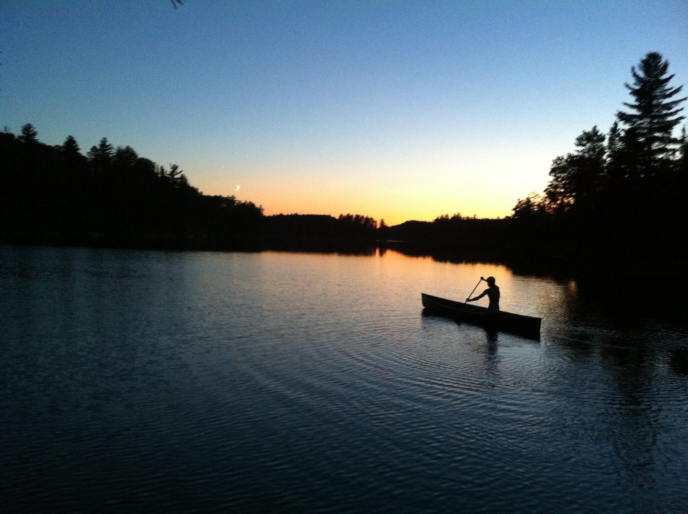 A camper paddling a canoe solo on a lake at sunset