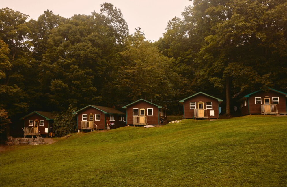 A row of dark cedar cabins with white trim among the pines at Kilcoo Camp