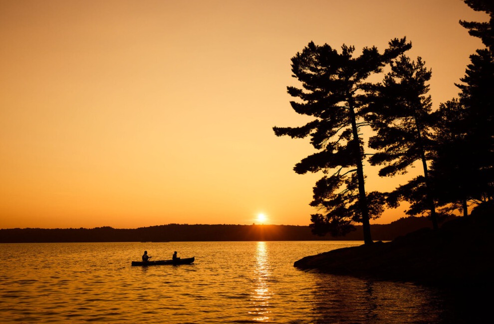 Sunset over Gull Lake with campers paddling a canoe