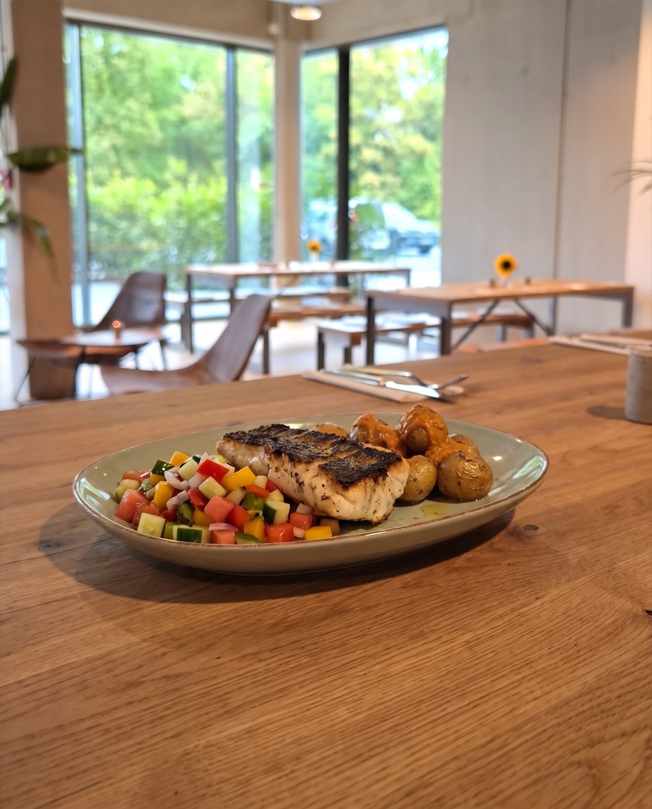 Gegrillter Fisch mit Gemüse und Kartoffeln auf hellem Tisch am Fenster