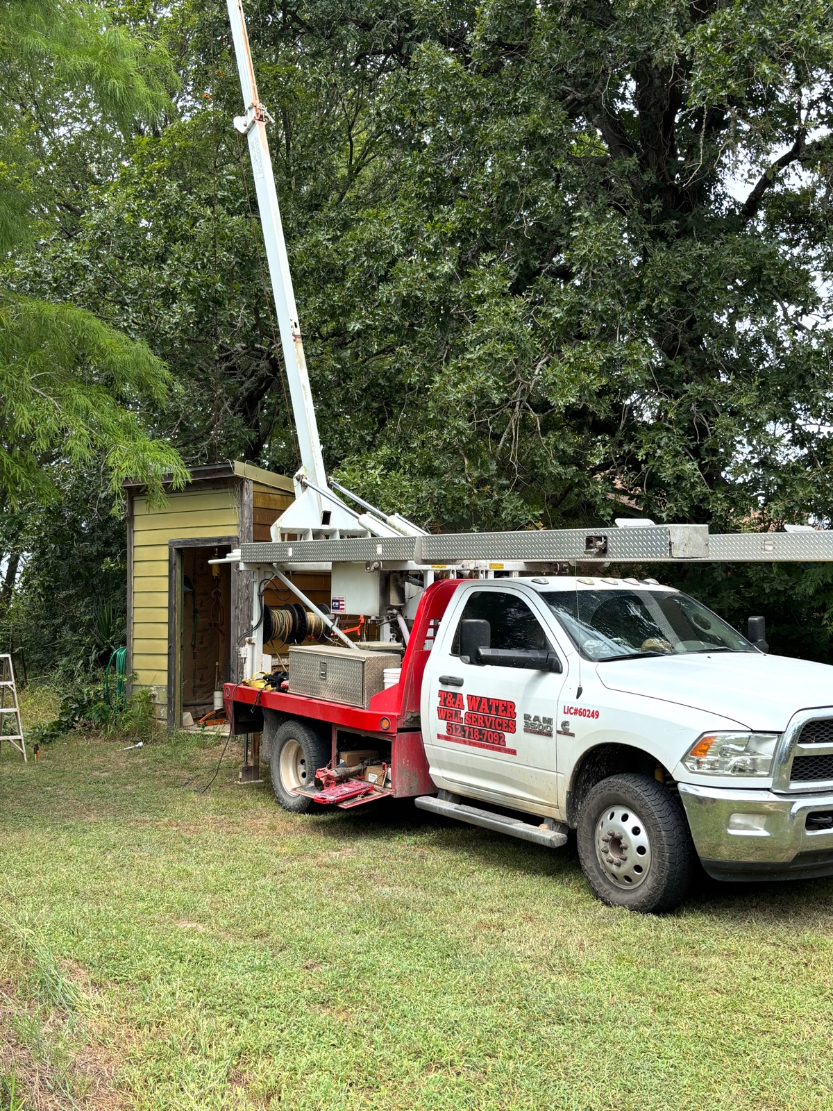 T&A service truck with boom raised at a rural well house
