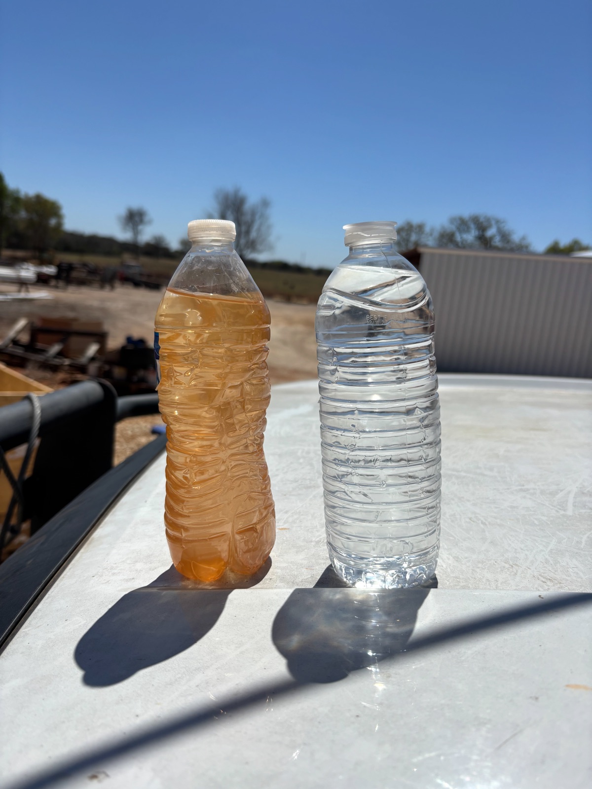 Cloudy untreated well water beside clear filtered water in two bottles