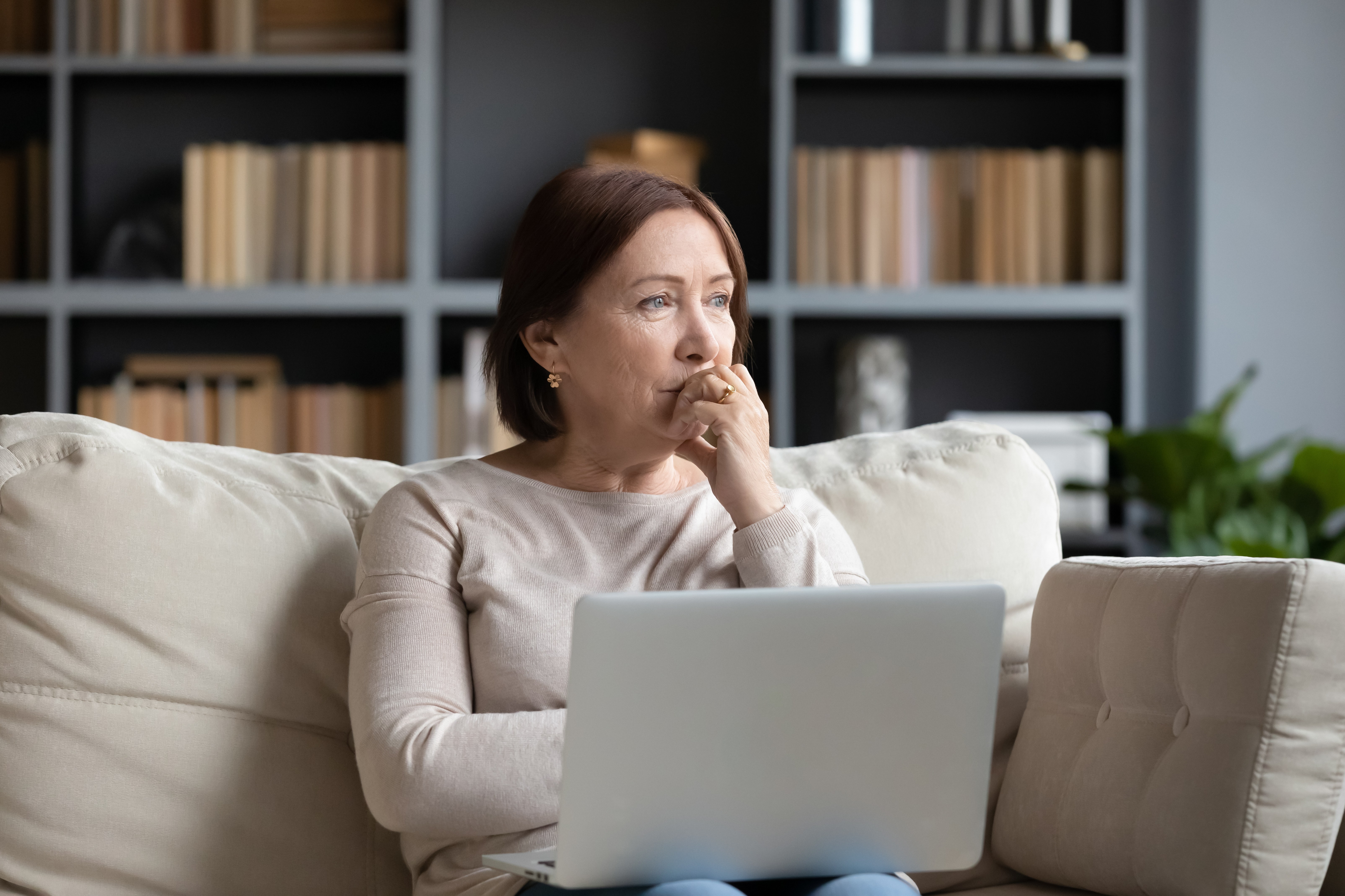 Woman sitting thoughtfully on a couch with a laptop