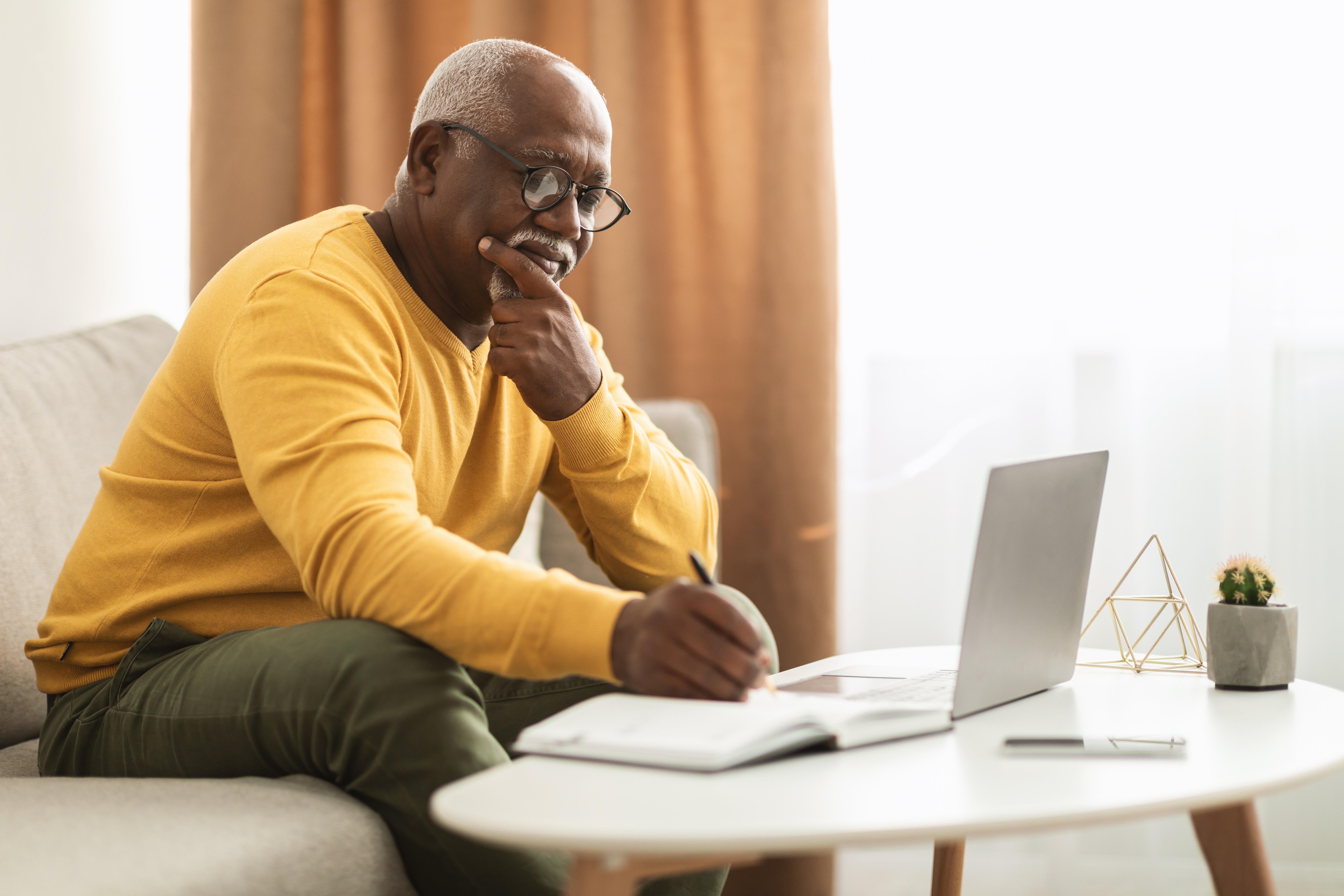 Man writing in a notebook next to a laptop
