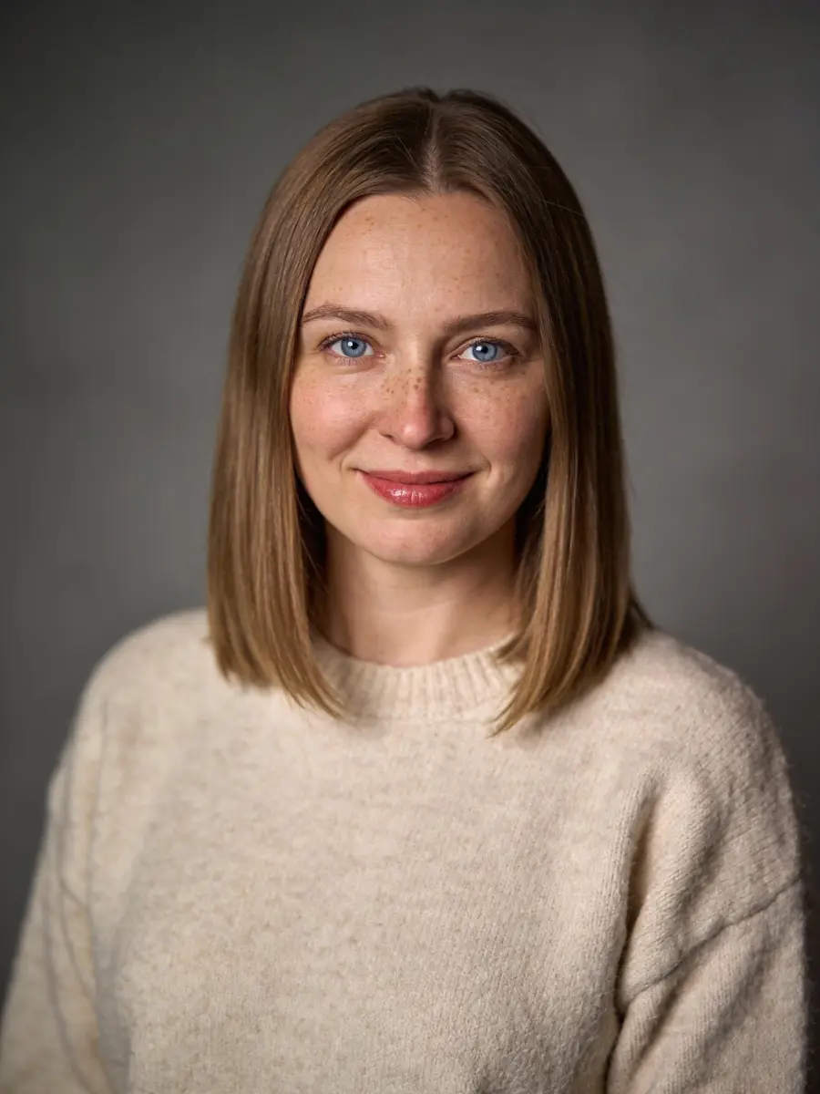 Portrait of a smiling woman with shoulder-length hair wearing a beige sweater against gray background.