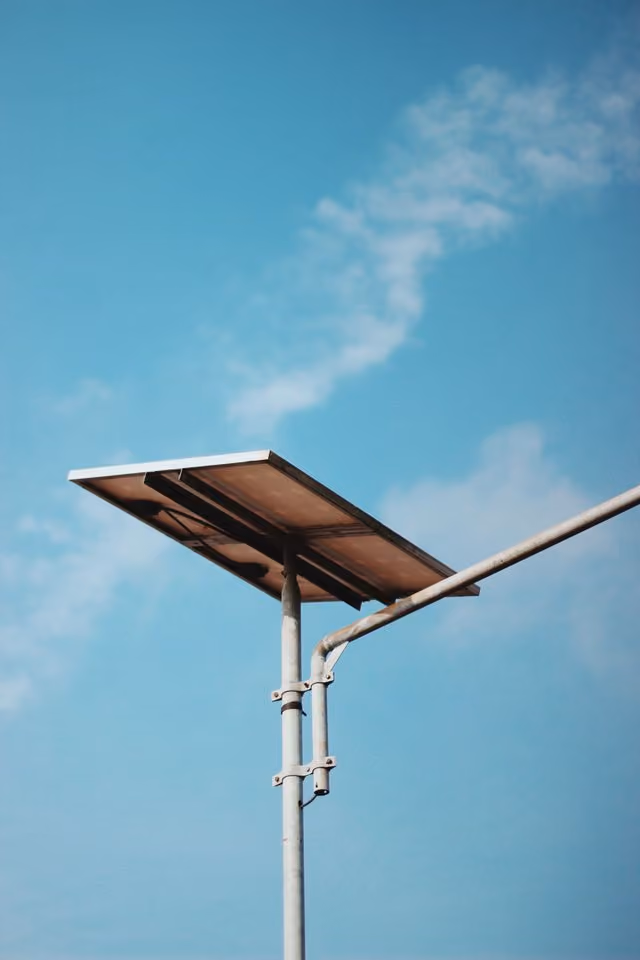Solar panel mounted on a pole against a clear blue sky with scattered clouds.
