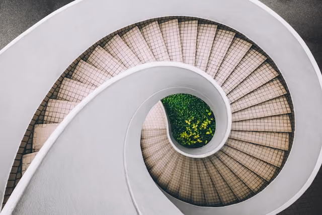 Top view of a spiral staircase with beige steps and green plants in the center.