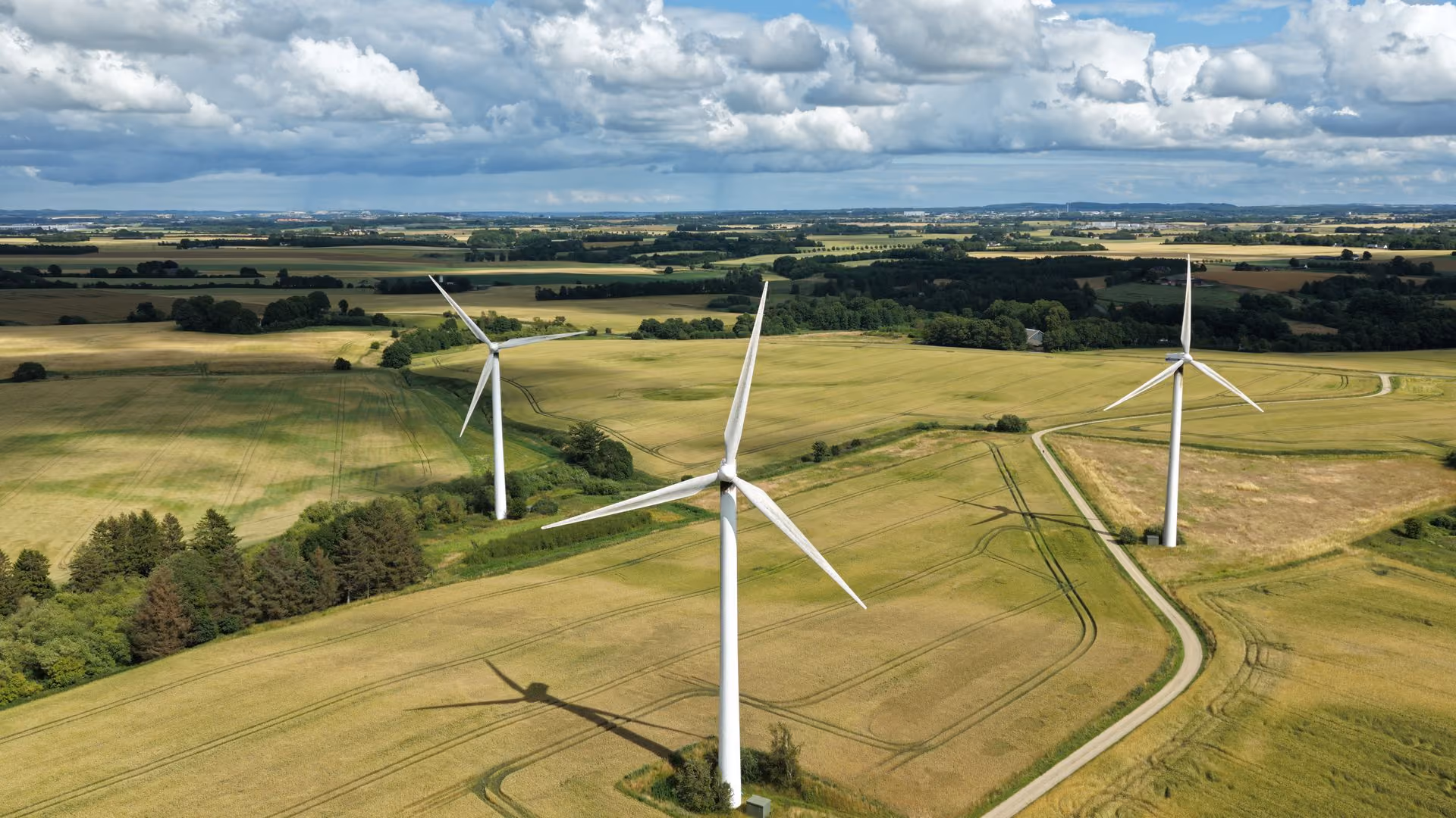 Aerial view of three wind turbines in a green field under a partly cloudy sky.