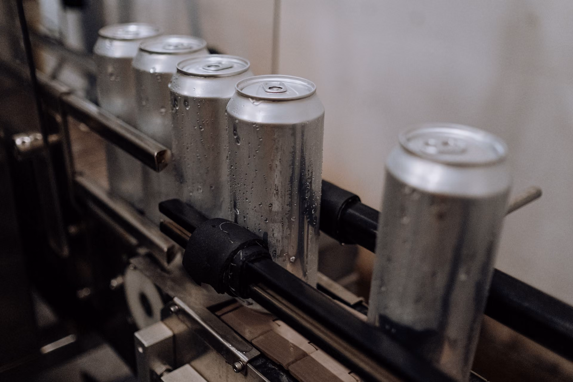 Row of chilled aluminum beverage cans with water droplets moving along a production line conveyor belt