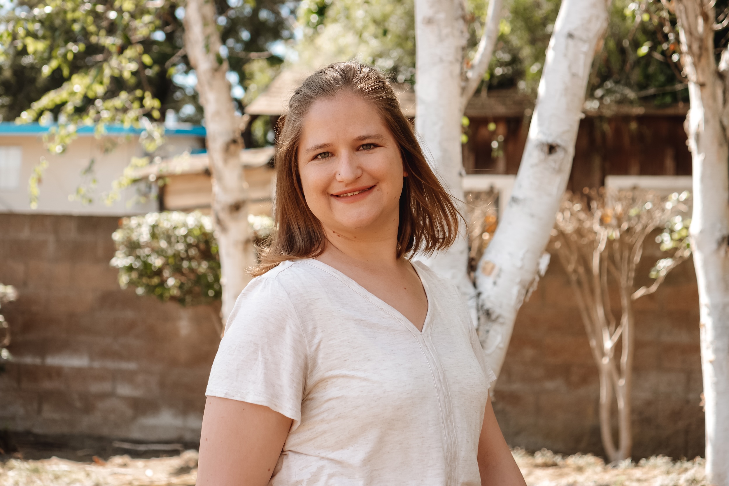 Hannah Ly, LMFT, smiling outdoors among birch trees, a child and teen therapist trained in play therapy and Brainspotting