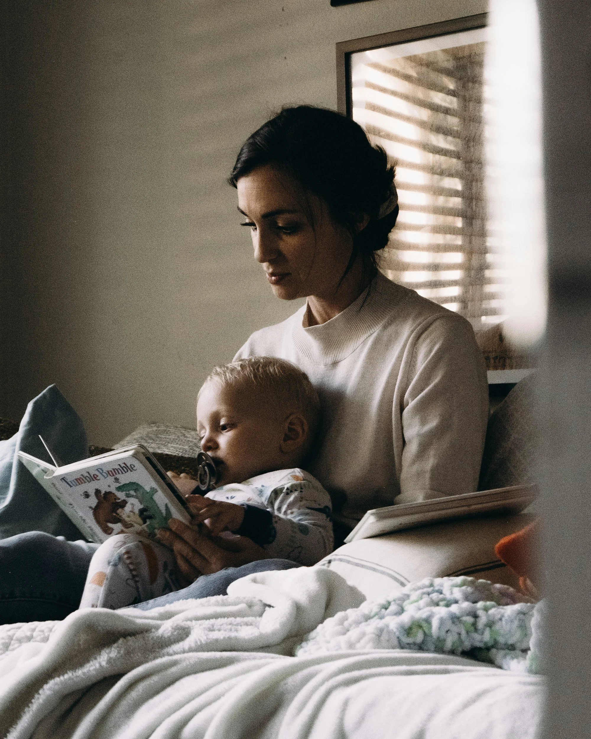 A mother reading a picture book with her baby in bed