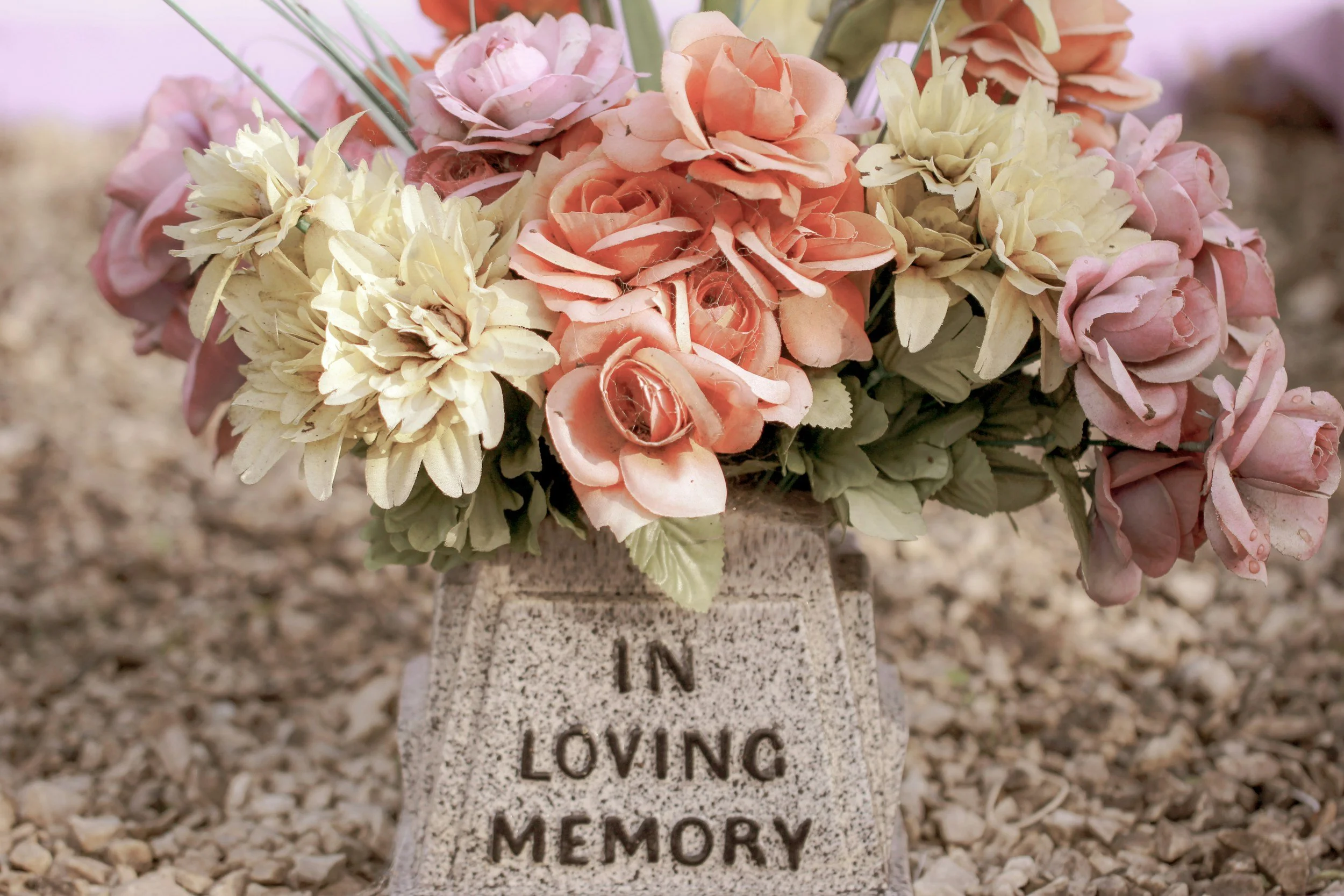 Pink and cream flowers in a stone planter engraved In Loving Memory