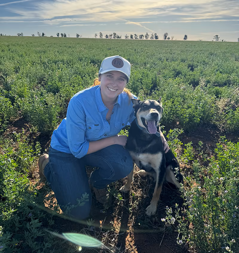 Dr Gabbie Forrest, Associate Veterinarian at Western Victoria Vets, kneeling in a crop paddock with her dog
