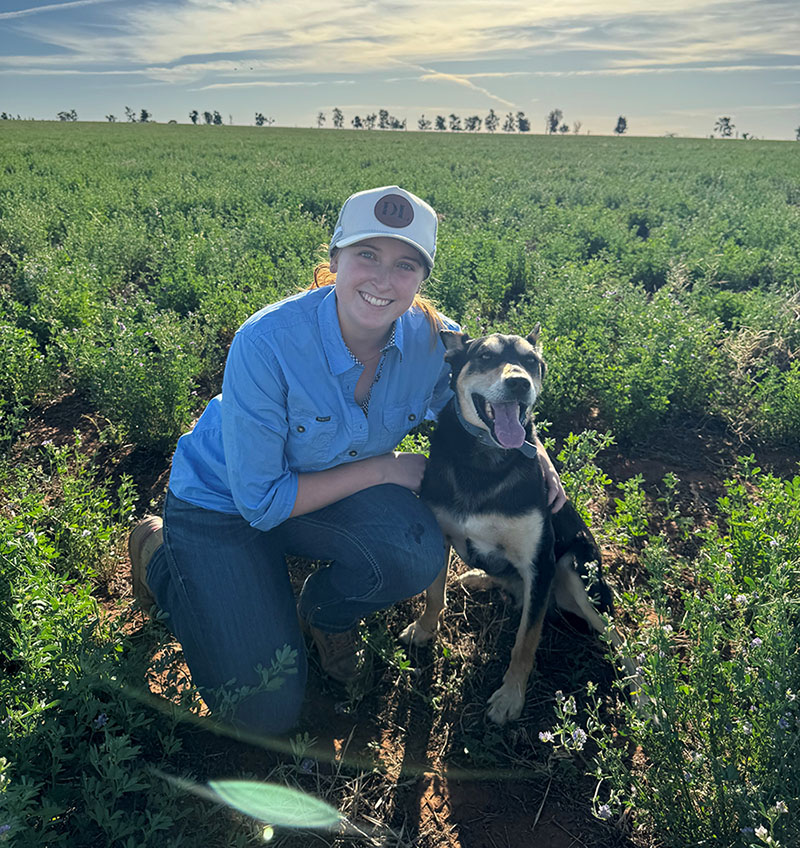Dr Gabbie Forrest, Associate Veterinarian at Western Victoria Vets, kneeling in a crop paddock with her dog