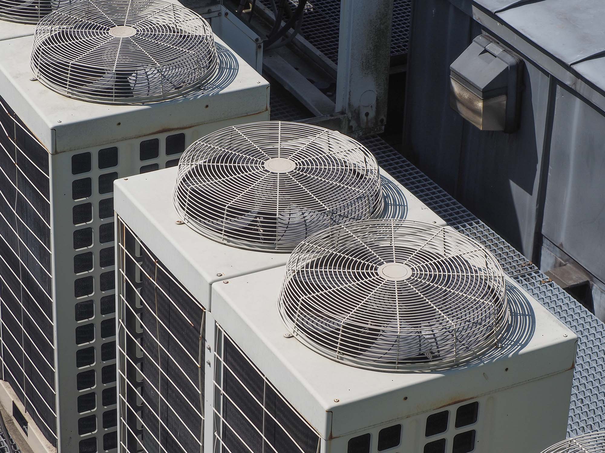Three industrial air conditioning units with protective fan grilles on top on a rooftop.