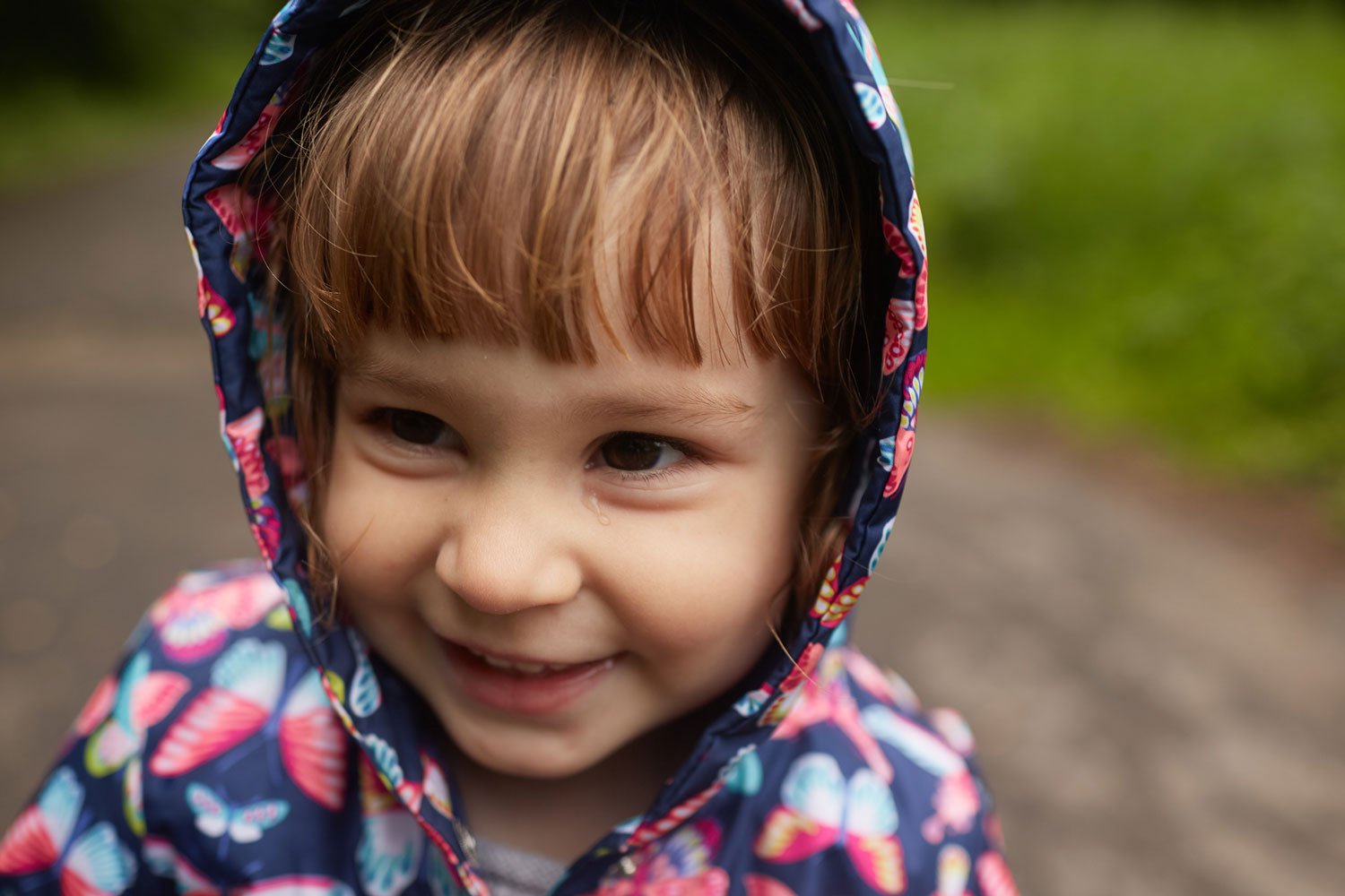 Smiling child with a tear on cheek wearing a blue butterfly-patterned hooded jacket.