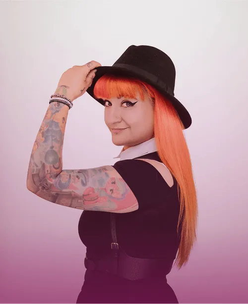 Frau mit rotem Haar, schwarzem Hut und tätowiertem Arm in schwarzem Kleid, lächelt über die Schulter auf pastellviolettem Hintergrund.