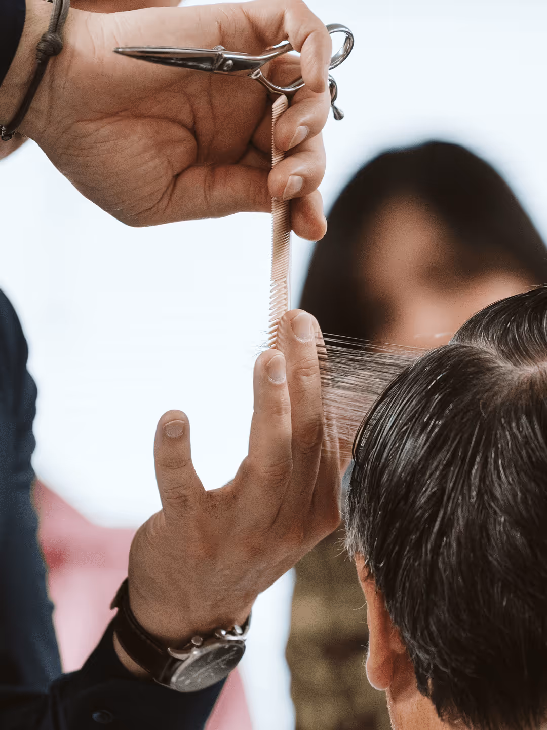 Friseur schneidet graues Herrenhaar mit Schere und Kamm; Nahaufnahme zeigt Handarbeit und Präzision.