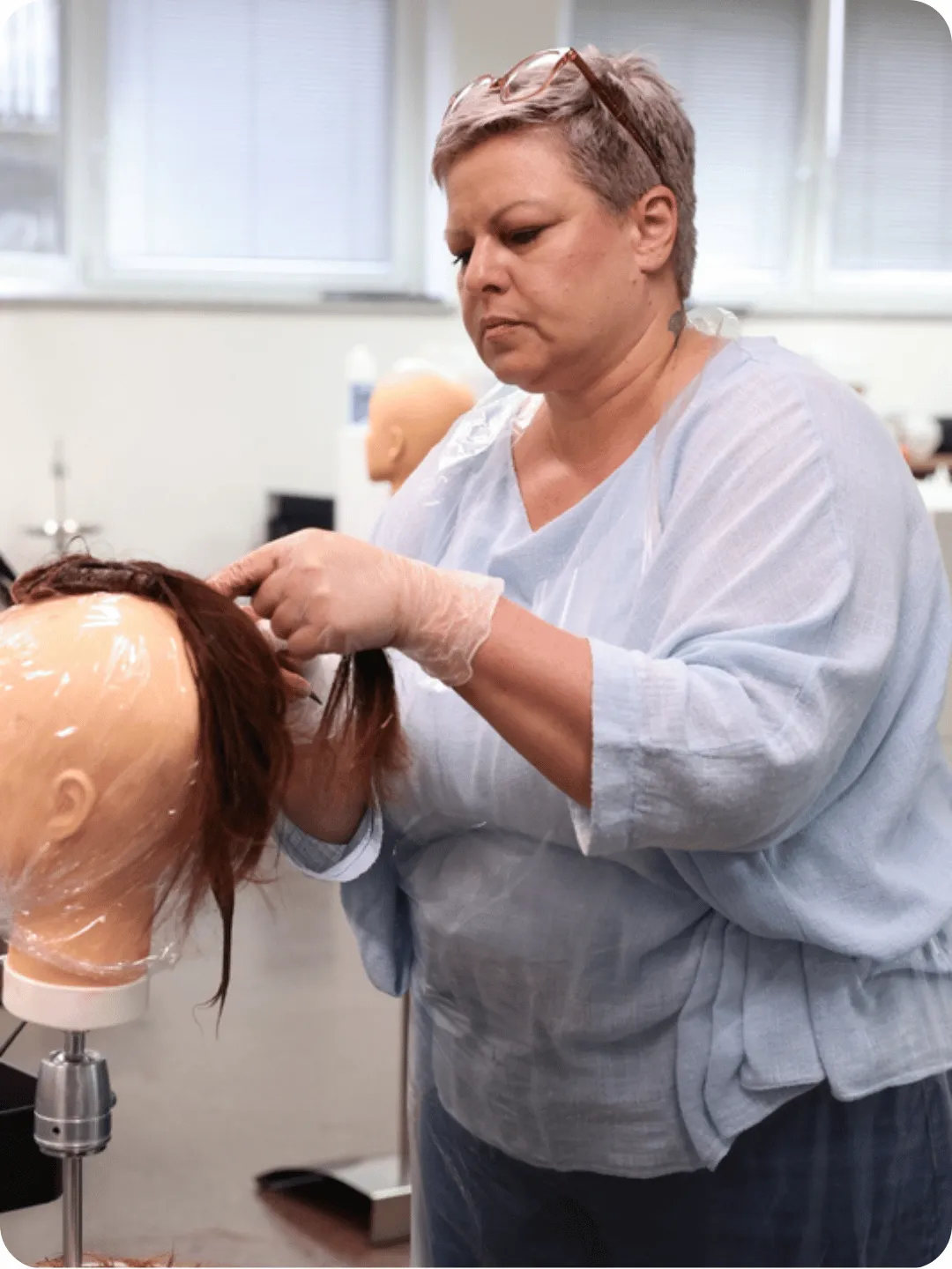 Teilnehmerin übt Haarverlängerung an einem Übungskopf im Schulungsraum der Deutschen Friseurakademie