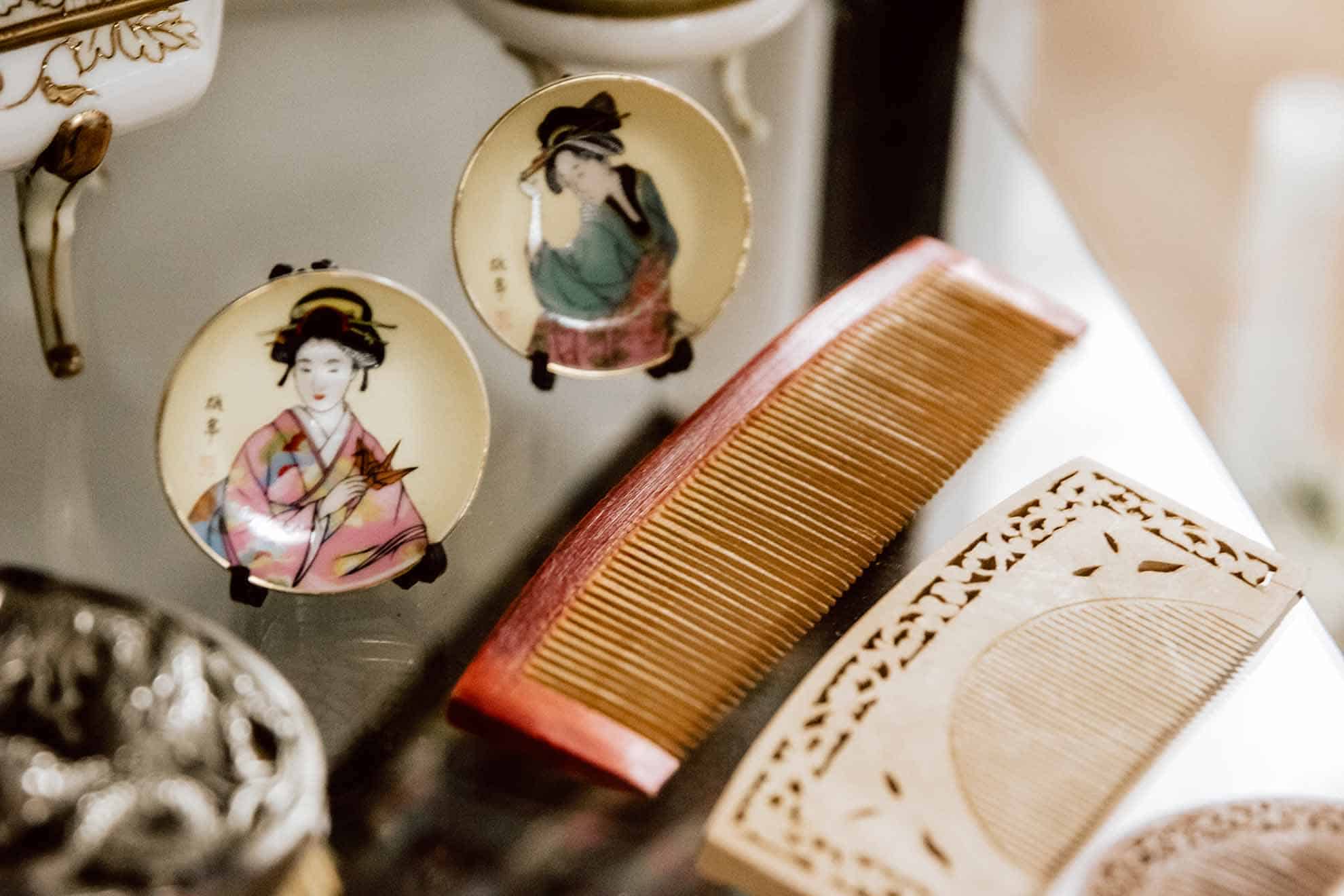 Historischer Holzkamm neben bemalten asiatischen Porzellantellern und einer geschnitzten Schatulle im Friseurmuseum