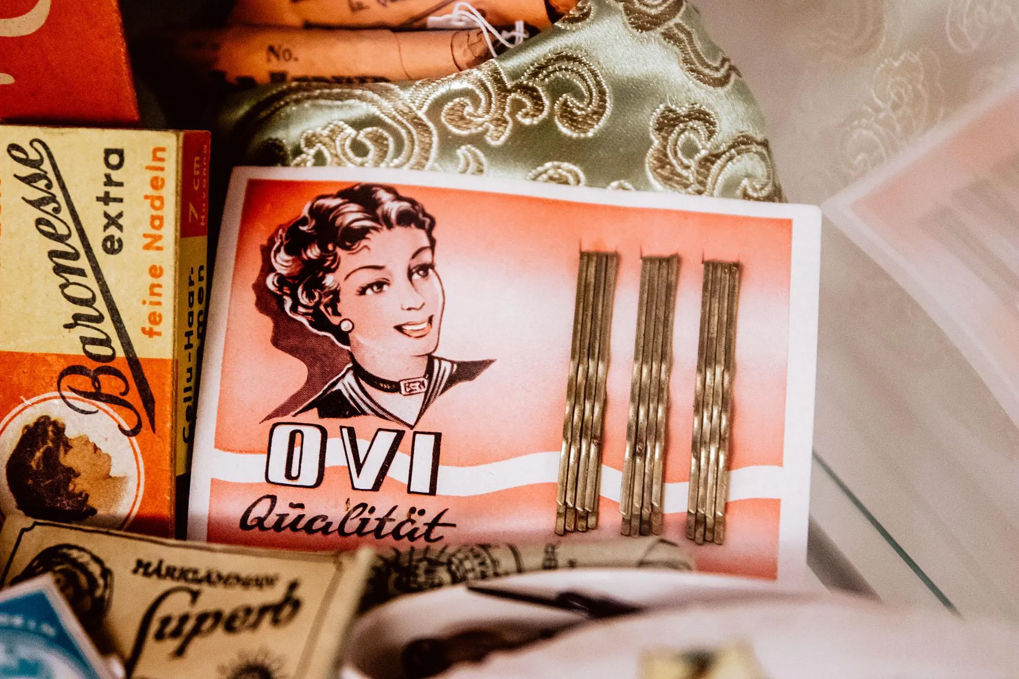 Historische Friseurartikel in einer Vitrine von Herr Zopf's Friseurmuseum, darunter Haarnadel-Verpackungen der Marke Baronesse