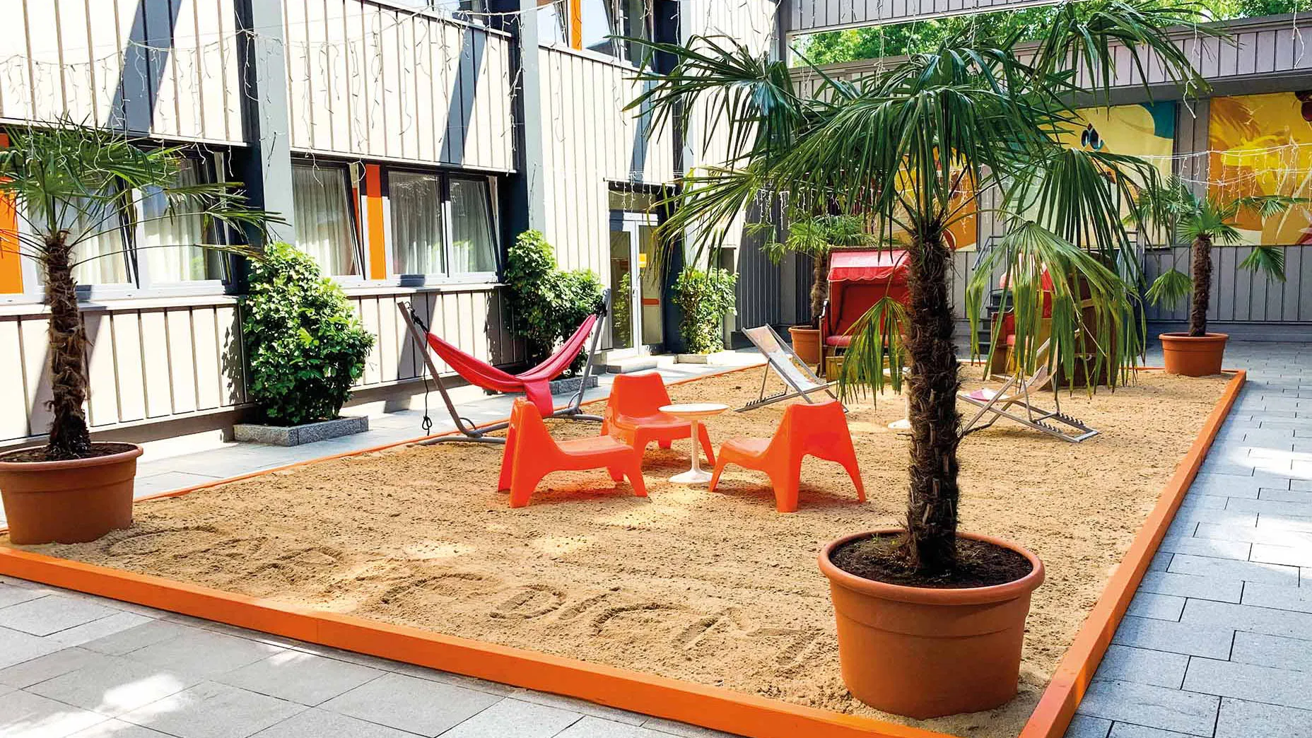 Beach Lounge des Orange Hotels in Neu-Ulm mit Sandfläche, Palmen und orangen Liegestühlen