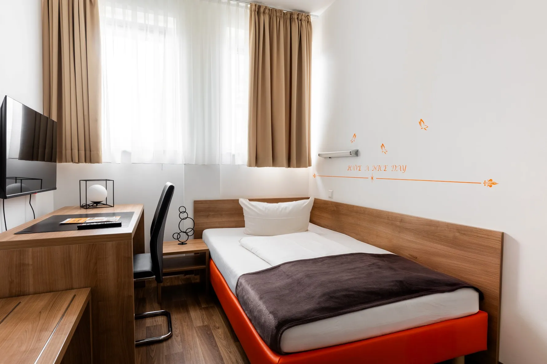 Hotelzimmer im Orange Hotel auf dem Friseurcampus Neu-Ulm mit Bett, Schreibtisch und Fernseher