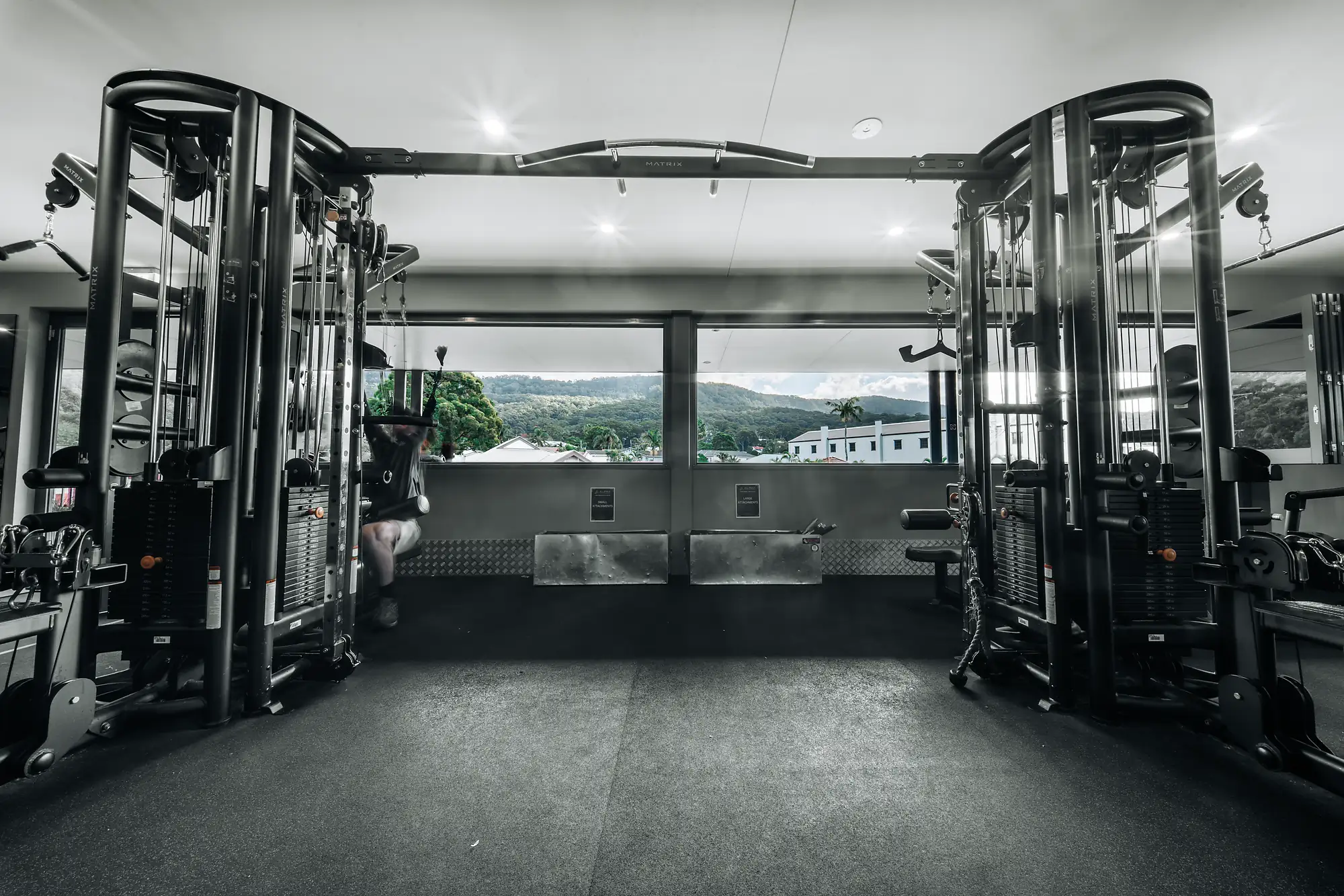 Modern gym with cable machines facing large windows showing mountains and buildings outside.