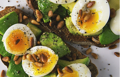 Close-up of avocado toast topped with soft boiled eggs and sprinkled with pine nuts and black pepper.