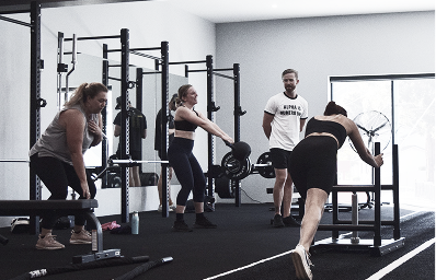 Women exercising with weights and a trainer supervising in a gym workout area.