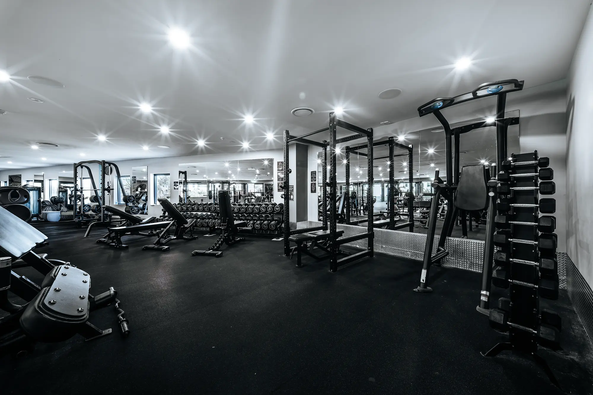 Modern gym with weight benches, dumbbells, and strength training machines under bright ceiling lights.
