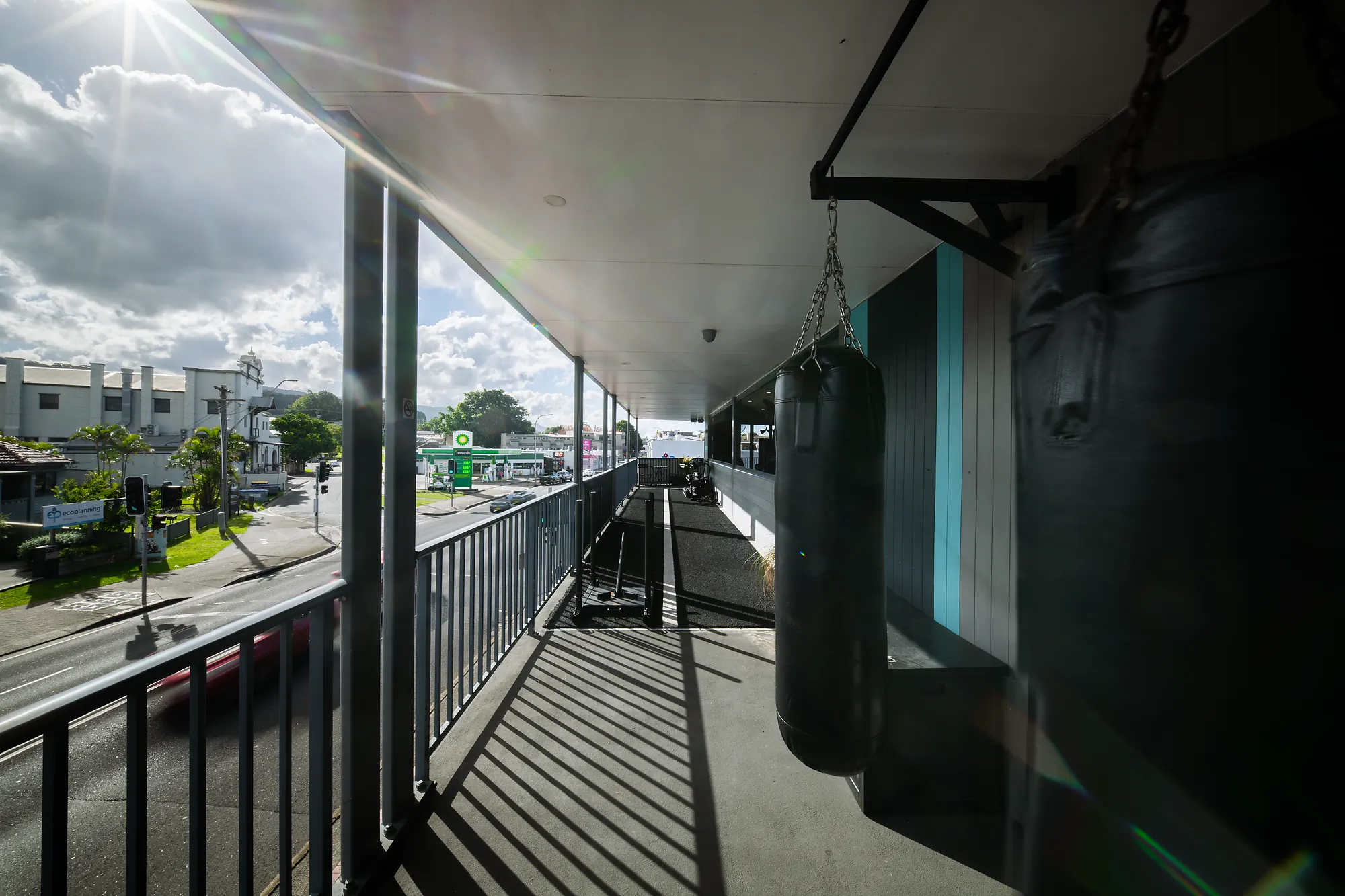 Outdoor balcony gym area with two hanging punching bags and sunlit street view.