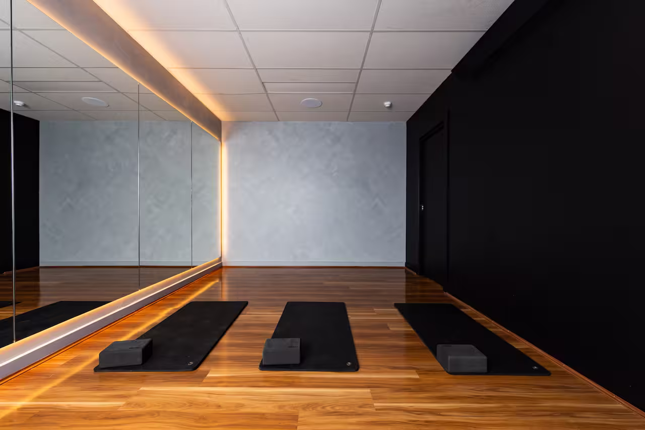 Interior of yoga studio with three black mats and blocks on wooden floor and large mirror wall.