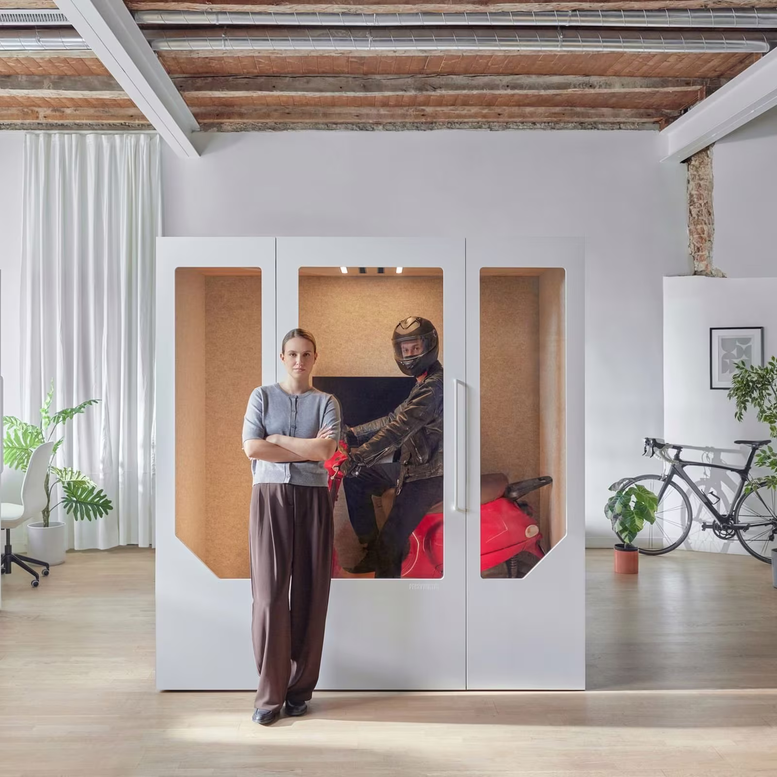 Woman standing next to a soundproof office booth with a person on a motorcycle inside