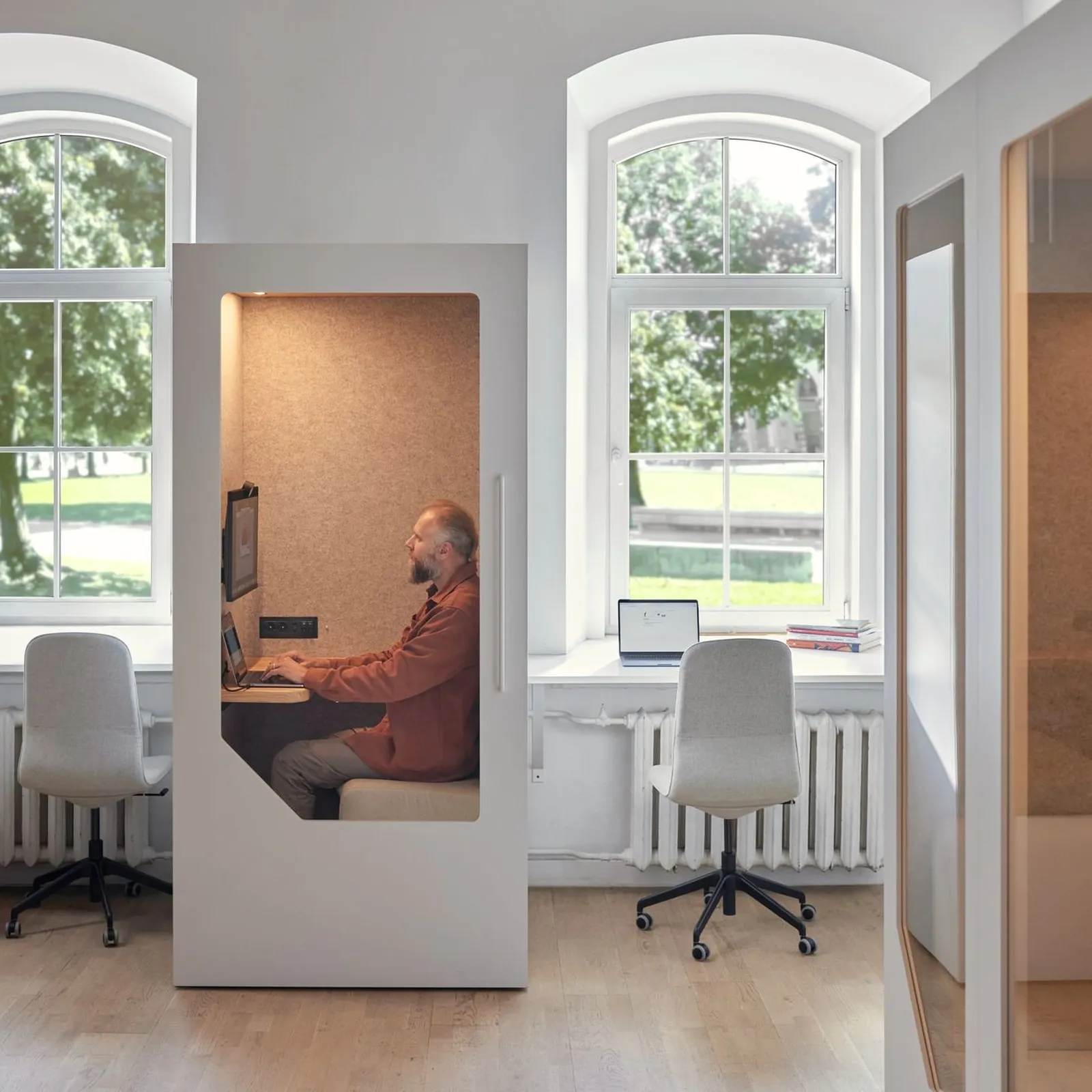 Person working focused inside a soundproof office pod in a bright open workspace