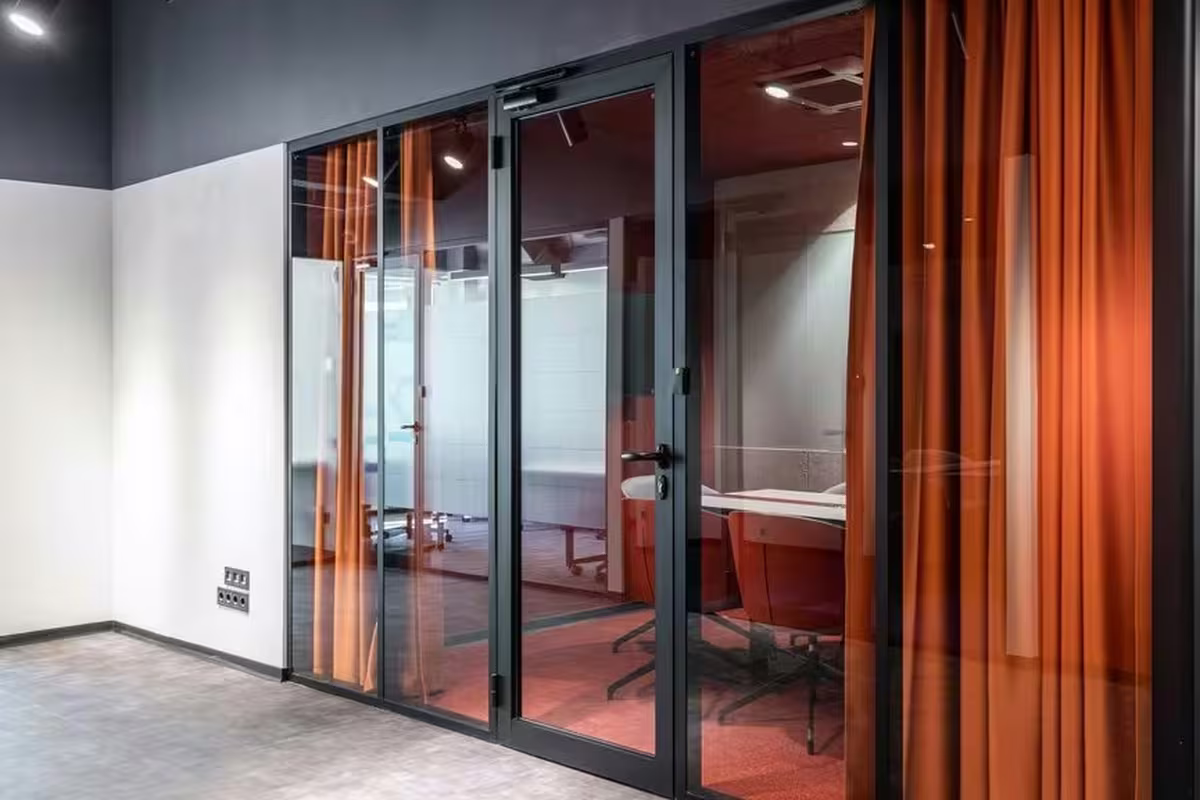 Glass-walled meeting rooms with orange acoustic curtains for privacy in an open office